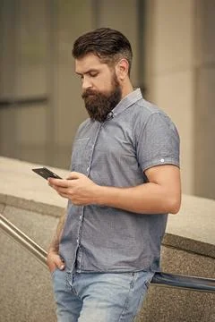 Bearded man using mobile phone device for mobile sms messaging outdoors, mobile Foto stock