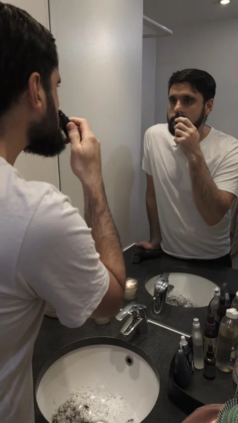 Bearded man using nose hair trimmer while looking in bathroom mirror Video stock 335636318