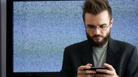 Bearded man using smartphone with grainy screen behind 库存影片 73738484