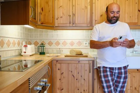 Bearded man using smartphone in kitchen Stock Photos