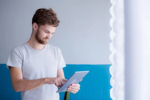 Bearded man using tablet while standing near the window in his modern apartme 写真素材