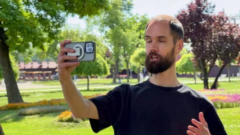 Bearded Man Vlogging with Smartphone in Sunny Palic Park Stock Footage 336178223