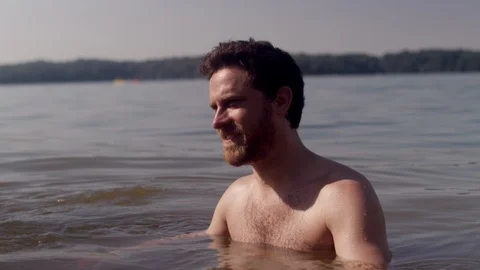 Bearded man wading in a forest lake talking to his friends on a summer day 스톡 동영상 116708076