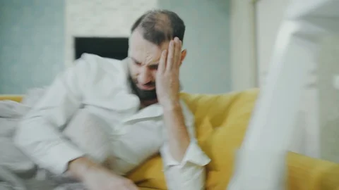 A bearded man wakes up after a night out, feels dizzy, hangover, splitting Stock Footage 99801311