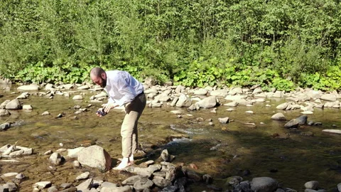 Bearded Man Washing Socks in Shallow Mountain River on Sunny Day Stock Footage 344887934