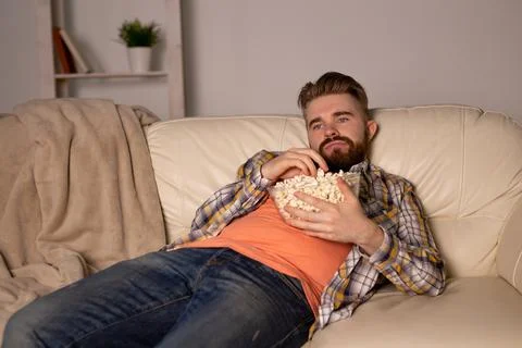 Bearded man watching film or sport games TV eating popcorn in house at night Stock Photos