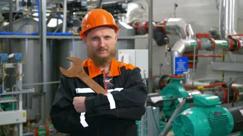 A bearded man at work, a mechanic in an orange helmet at his workplace in an Stock Footage 170705323