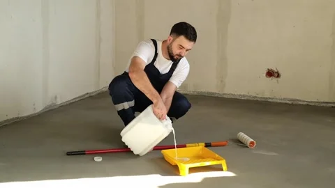 A bearded man in a work uniform is pouring the ready-made primer into a special Stock Footage 318879572