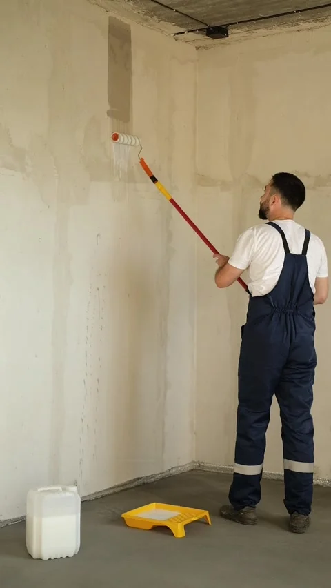 A bearded man in a work uniform is priming the walls after applying gypsum Stock Footage 318879522