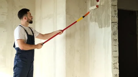 A bearded man in a work uniform is priming the walls after applying gypsum Stock Footage 318879626