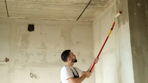 A bearded man in a work uniform is priming the walls after applying gypsum Stock Footage 318896983