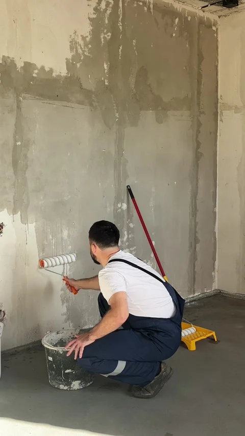 A bearded man in a work uniform is priming the walls after applying gypsum Stock Footage 346693363