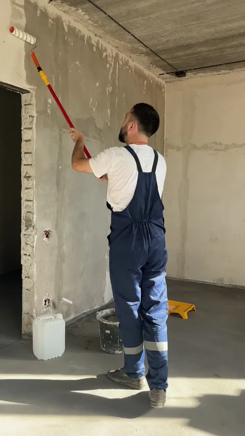 A bearded man in a work uniform is priming the walls after applying gypsum Stock Footage 346693539