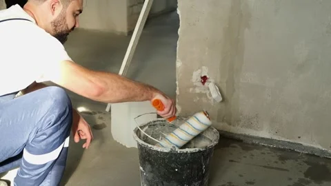 A bearded man in a work uniform is squeezing out the roller in the bucket, he is Stock Footage 318879490