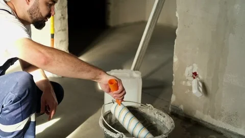 A bearded man in a work uniform is squeezing out the roller in the bucket, he is Stock Footage 318897002