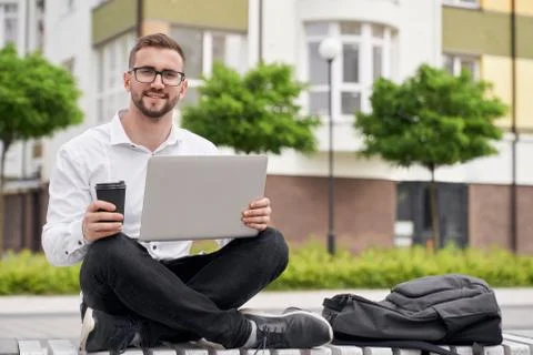 Bearded man working, sitting on bench with crossed legs. Stock Photos