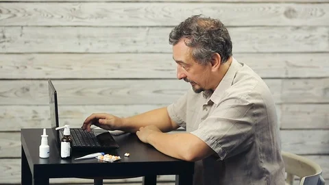 A bearded man works at the computer and coughs. Stock Footage 98759963