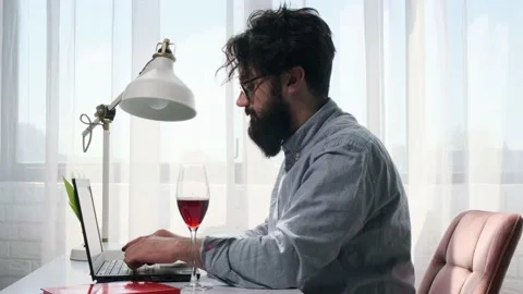Bearded man that works at the computer full of reminder notes, drink wine. Stock Footage 153482229