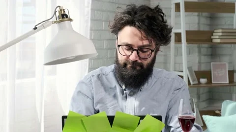 Bearded man that works at the computer full of reminder notes, drink wine. Stock Footage 155404773