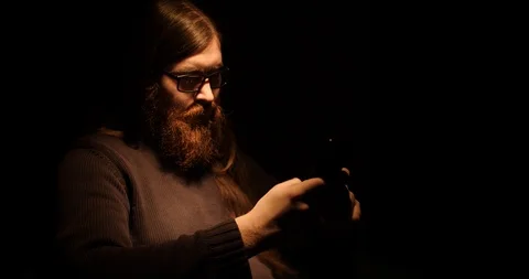 Bearded man writes an SMS in a dark room Stock Footage 88060545