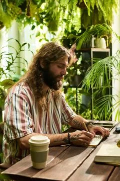 Bearded Man Writing in Notebook While Working in Green Cafe Fotos de archivo