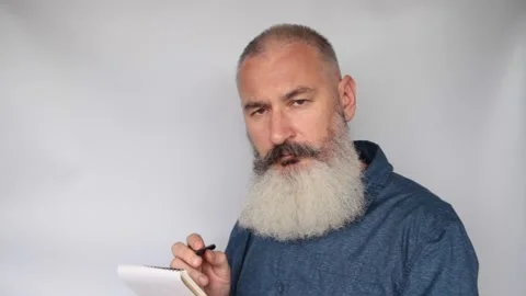Bearded mature man looks at camera, listens to client and takes notes Stock Footage 132213587