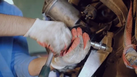 The bearded mechanic tightens the bolt with a tool on the hull of an automotive Stock Footage 78831056