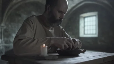 Bearded medieval man breaking bread over a wooden bowl and eating it Stock Footage 340079647