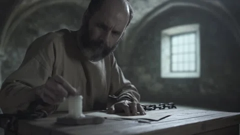 Bearded medieval man in iron cuffs extinguishing a burning candle with fingers 스톡 동영상 339631373