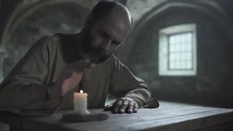 Bearded medieval man looking at burning candle and warming his hand over flame Stock Footage 341467398