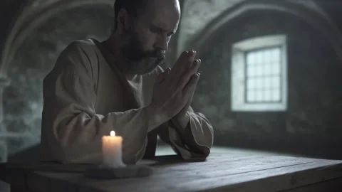 Bearded medieval man praying with closed eyes and palms together at a table Stock Footage 339232012