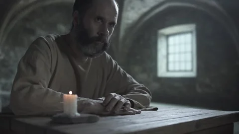 Bearded medieval prisoner scratching his arm and raising a wary look aside Stock Footage 342016558