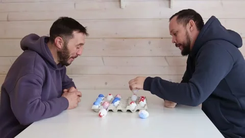 Bearded men play chess with Easter eggs at white table. Creative ideas for Stock Footage 234448800