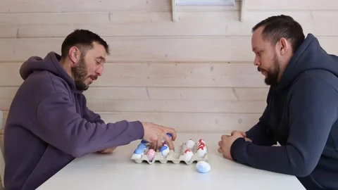 Bearded men play chess with Easter eggs at white table. Creative ideas for Stock Footage 234926922