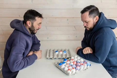 Bearded men play chess with Easter eggs at white table. Creative ideas for Stock Photos