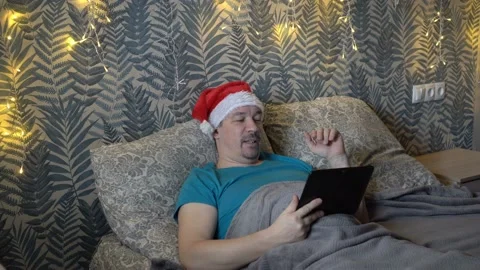 A bearded middle-aged man communicates via video link via a tablet, lying on a Video stock 148448484