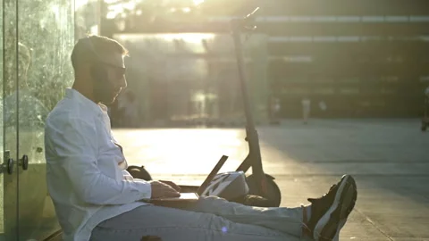 Bearded middle-aged man in dark glasses sits on the sidewalk with a laptop Stock Footage 207539655