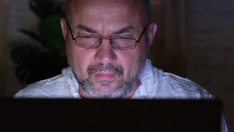 Bearded middle aged man in glasses wearing white shirt using computer at night Video stock 274223684
