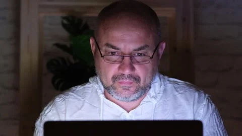 Bearded middle aged man in glasses working on laptop on online project at night Stock Footage 276465519