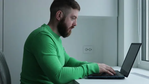 Bearded middle aged man in green t-shirt using laptop computer Stock Footage 180415760
