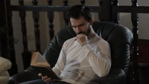 Bearded Middle Aged Man Reading a Book Indoors on an Armchair Stock Footage 237874542