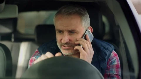 A bearded middle-aged man sits in a car and talks on the phone. A gray-haired Stock Footage 242604972
