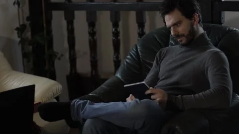 Bearded Middle Aged Man Writing in a Notebook Indoors on an Armchair Stock Footage 237874529