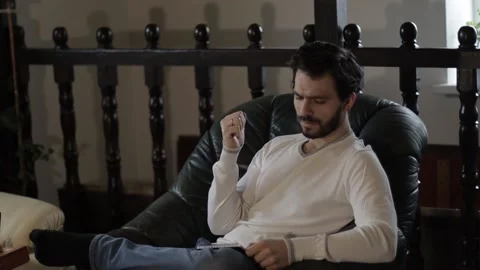 Bearded Middle Aged Man Writing in a Notebook Indoors on an Armchair Stock Footage 237874549