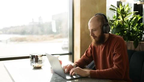 Bearded millennial man developer working at cafe, using laptop computer and.. Stock Photos
