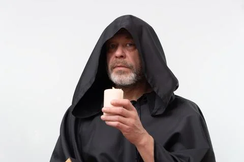 Bearded monk in hood looking forward holding candle and book. Photos
