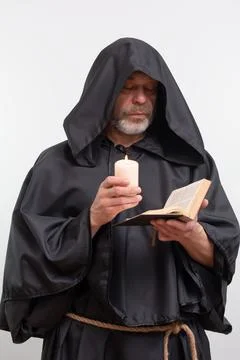 Bearded monk in hood reading text by candle light. 写真素材