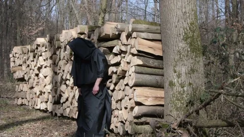A bearded monk in a long robe barefooted throws a log on a stack of firewood in  Stock Footage 303710351