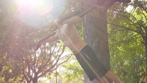 Bearded muscular man doing workout excercises on fitness loops near a tree. 4K Stock Footage 98467905