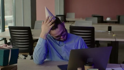 Bearded office worker in cone at workplace with laptop and gift  Stock Footage 271196941